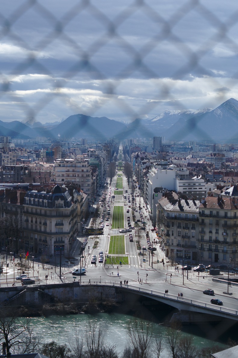 A vertical of Grenoble with a wire fence in the foreground.