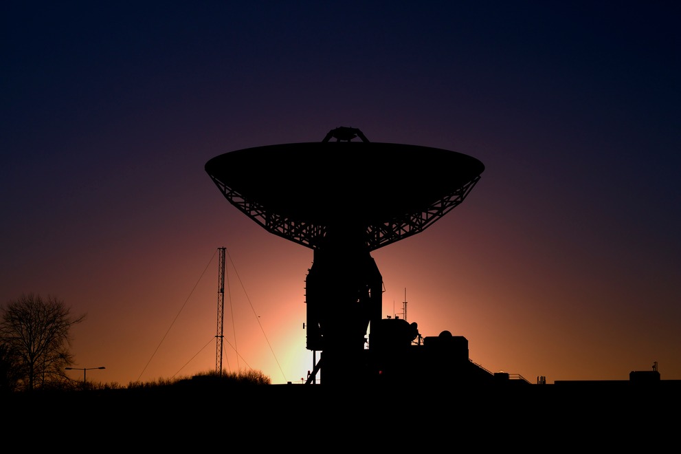 A colorful sunset behind a radio telescope.